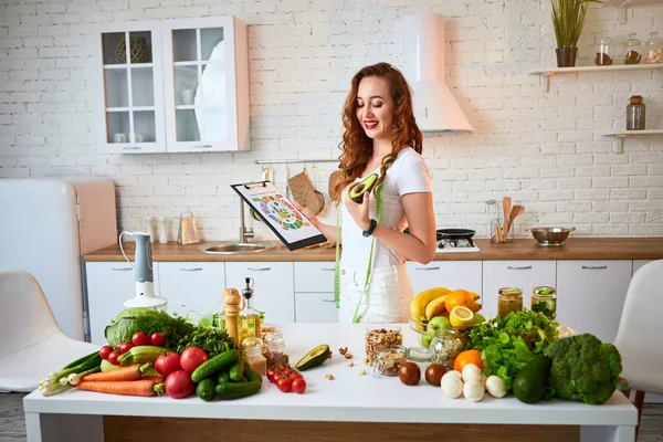 Young beautiful woman using tablet with infographic while cooking in the modern kitchen. Healthy eating, vitamins, dieting, technology and people concept. Losing Weight