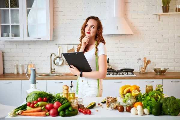 Young beautiful woman using tablet while cooking in the modern kitchen. Healthy eating, vitamins, dieting, technology and people concept. Losing Weight