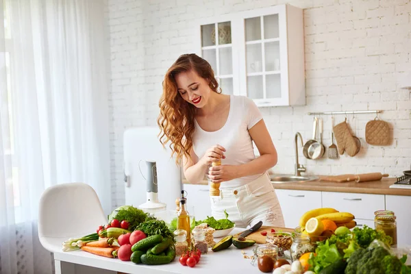 Tânăra femeie fericită pregătește salată gustoasă în bucătăria frumoasă cu ingrediente proaspete verzi în interior. Alimente sănătoase și conceptul de dietă. Pierdere în greutate — Fotografie, imagine de stoc