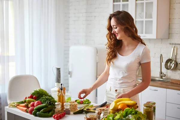 Mladá šťastná žena připravuje chutné saláty v nádherné kuchyni se zelenými čerstvými ingrediencemi uvnitř. Zdravá strava a dieting koncepce. Uvolňující váha — Stock fotografie