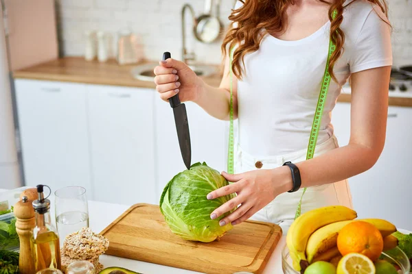 Νέα χαρούμενη γυναίκα κοπή λάχανο για την κατασκευή σαλάτα στην όμορφη κουζίνα με πράσινα φρέσκα υλικά σε εσωτερικούς χώρους. Υγιεινά φαγητά και δίαιτες. Χάνοντας βάρος — Φωτογραφία Αρχείου