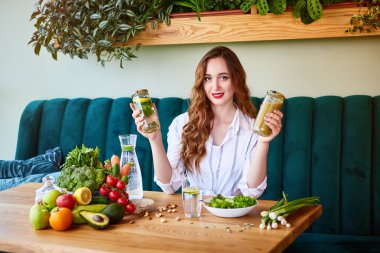 Masanın üzerinde arka plan ve taze meyve ve sebzeler üzerinde yeşil çiçekler ile güzel iç Smoothie ve taze su içme genç kadın. Sağlıklı yeme konsepti. Vegan yemek ve Detox menüsü