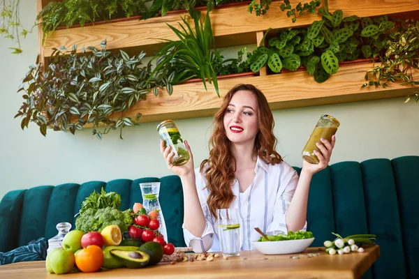 Masanın üzerinde arka plan ve taze meyve ve sebzeler üzerinde yeşil çiçekler ile güzel iç Smoothie ve taze su içme genç kadın. Sağlıklı yeme konsepti. Vegan yemek ve Detox menüsü