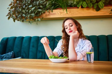 Masanın üzerinde arka plan ve taze malzemelerle yeşil çiçekler ile güzel iç salata yiyen genç mutlu kadın. Sağlıklı gıda konsepti