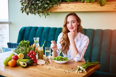 Masanın üzerinde arka plan ve taze malzemelerle yeşil çiçekler ile güzel iç salata yiyen genç mutlu kadın. Sağlıklı gıda konsepti