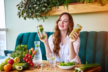 Genç kadın arka plan ve taze meyve ve sebzeler üzerinde yeşil çiçekler ile güzel iç Smoothie ve taze su içme. Sağlıklı yeme konsepti. Vegan yemek ve Detox menüsü