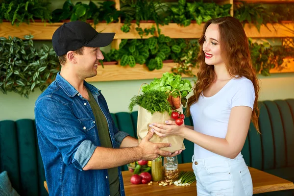 Курьер доставляет свежую еду, дарит сумку счастливой клиентке на кухне дома. Онлайн-покупки продуктов питания из Интернета - магазин — стоковое фото