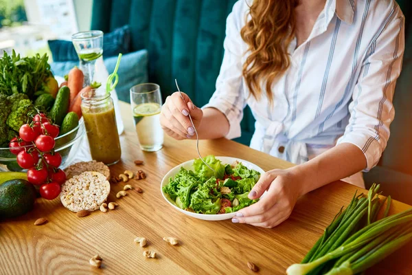 배경에 녹색 꽃과 테이블에 신선한 재료와 아름다운 인테리어에 샐러드를 먹고 젊은 행복한 여성. 건강한 음식 개념 — 스톡 사진