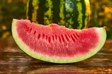 Bulanık bahçe günbatımı arka plan ile ahşap masa üzerinde Taze olgun çizgili dilimlenmiş karpuz. Gıda, Meyve veya sağlık konsepti.