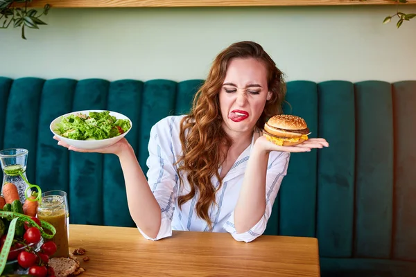 かわいい女性は不健康なハンバーガーを食べることを拒否しています。彼女は嫌悪感を持ってそれを見ている — ストック写真