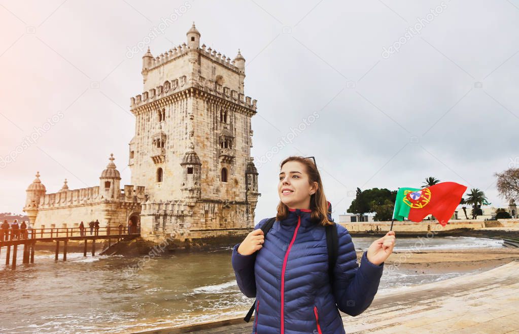 Young woman tourist walking near Belem tower holding the flag of Portugal in hands on the riverside in Lisbon