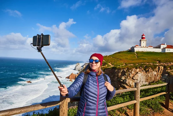 Young woman tourist at Cape Caba da Roca take a selfie shoots with view on beautiful landscape on a mobile phone, winter trip to Portugal. Westernmost point of Europe — Stock Photo, Image