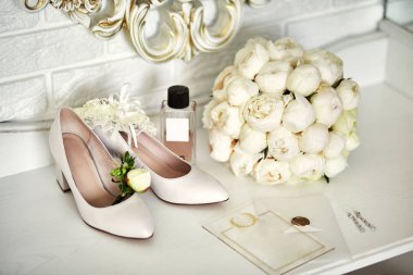Ayakkabı, buket, yüzük ve parfüm gibi düğün aksesuarları bir masanın üzerinde bulunur.