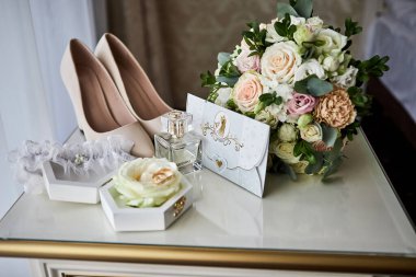Bir masada ayakkabı, buket, yüzük ve parfüm gibi düğün aksesuarları.