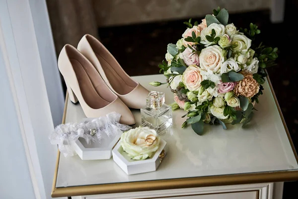 bridal accessories such as shoes, bouquet , ring and parfume on a table