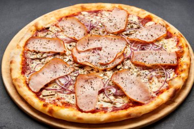 Lezzetli İtalyan pizzası, jambon, soğan ve koyu arkaplanda mozzarella peyniri.