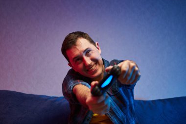 Çılgın oyuncu portresi, video oyunları oynayan çocuk kanepede oturuyor, konsol oyun platformunu elinde tutuyor. Evde dinlenmek, iyi hafta sonları.