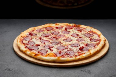 Koyu arkaplanda mozzarella peyniri ve salamlı nefis İtalyan pizzası.