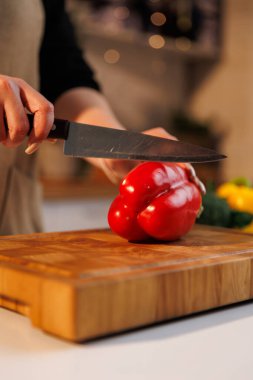 Ev mutfağında kırmızı dolma biberi dilimleyen bir kadın.