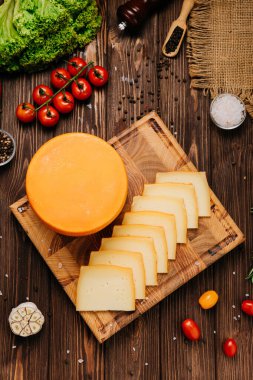 Köy tahtasında dilimlenmiş tam peynirli tekerlek, sebze ve otlarla servis ediliyor. Yüksek kalite fotoğraf