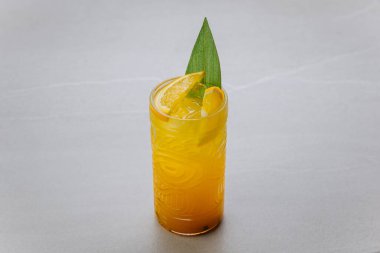Turuncu dilimli tropik sarı kokteyl ve gri arka planda palmiye yaprağı süslemesi. Yüksek kalite fotoğraf