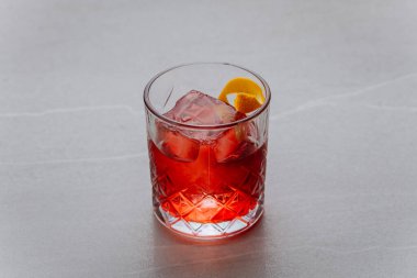 Gri arka planda kristal bir bardakta buz küpleri ve turunçgil bükülmüş klasik kırmızı kokteyl. Yüksek kalite fotoğraf