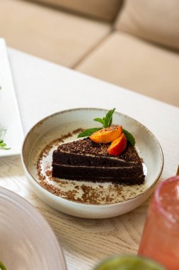 Şeftalili ve naneli bir dilim çikolatalı pasta tabakta servis edilir, doğal ışıkta yakın plan. Yüksek kalite fotoğraf
