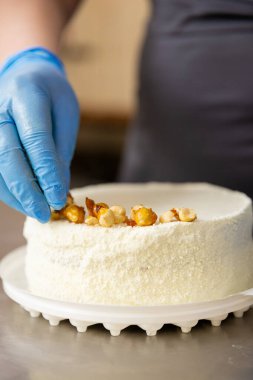 Pasta şefi, gıda üretim mutfağında beyaz fındıklı keki elle dekore ediyor. Yüksek kalite fotoğraf