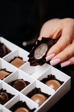 Manikürlü tırnakları olan bir kadının elindeki zarif kutuda bulunan lüks el yapımı çikolatalar. Yüksek kalite fotoğraf