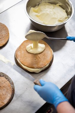 Pasta şefi, profesyonel fırın mutfağında pasta katmanına krema sürüyor, yakın plan. Yüksek kalite fotoğraf