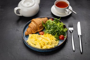 Sağlıklı kahvaltı, çırpılmış yumurta, kruvasan ve koyu arkaplanda taze salata. Yüksek kalite fotoğraf