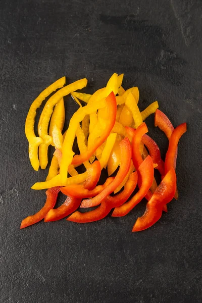 Taze dilimlenmiş kırmızı ve sarı dolmalık biber şeritleri, siyah kaplama arka plan, üst manzara. Yüksek kalite fotoğraf