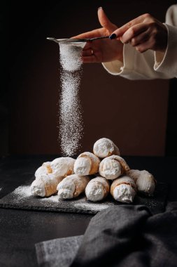 Taze krema boynuzları koyu arka planda pudra şekeriyle tozlanıyor, kış tatlıları gibi. Yüksek kalite fotoğraf