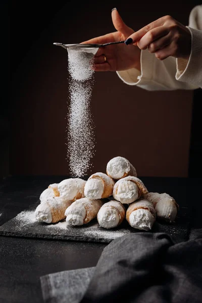 Taze krema boynuzları koyu arka planda pudra şekeriyle tozlanıyor, kış tatlıları gibi. Yüksek kalite fotoğraf