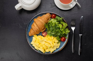 Sağlıklı kahvaltı, çırpılmış yumurta, kruvasan ve koyu arkaplanda taze salata. Yüksek kalite fotoğraf