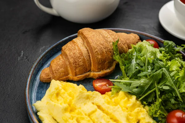 Sağlıklı kahvaltı, çırpılmış yumurta, kruvasan ve koyu arkaplanda taze salata. Yüksek kalite fotoğraf