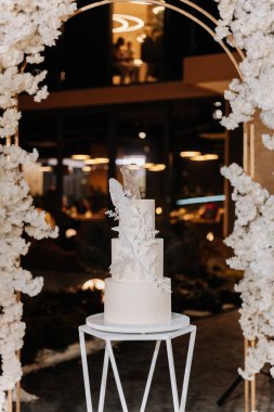 Lüks resepsiyonda modern stantta şekerli çiçek desenli zarif beyaz düğün pastası. Yüksek kalite fotoğraf