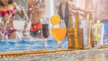 bikinili bulanık insanların arka planında yüzme havuzuna kurulmuş egzotik kokteyller ve bir şişe birayla içecek ve meyve suyu.