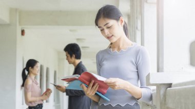 gülen kız portresi bir kırmızı kitap tutan ve mavi kitap, arka plan bulanıklık koridor açık öğrenci insanlar