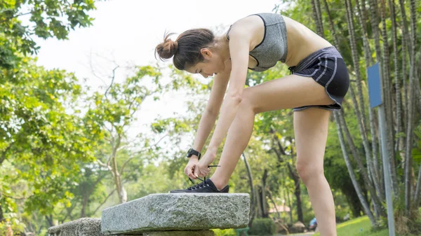 Asian cute sport healthy fit and firm slim teen girl in sport wear knot the shoe lacings in stone bench at outdoor garden