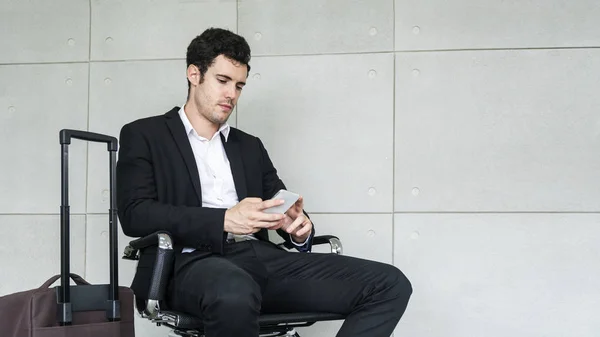 商务男士坐在椅子上等待商务旅行与手提箱和电话智能手机 — 图库照片