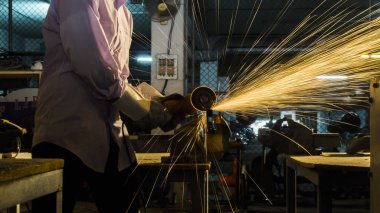 İşçi, kesik metali öğütüyor, düşük ışıkta parlak kıvılcımlara odaklanıyor.