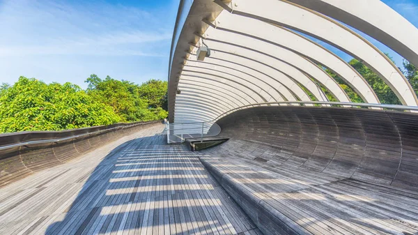 Çelik yapılı ahşap köprü yolu güneş ışığından yeşil çayıra ve mavi gökyüzü bulutuna kadar uzanır.
