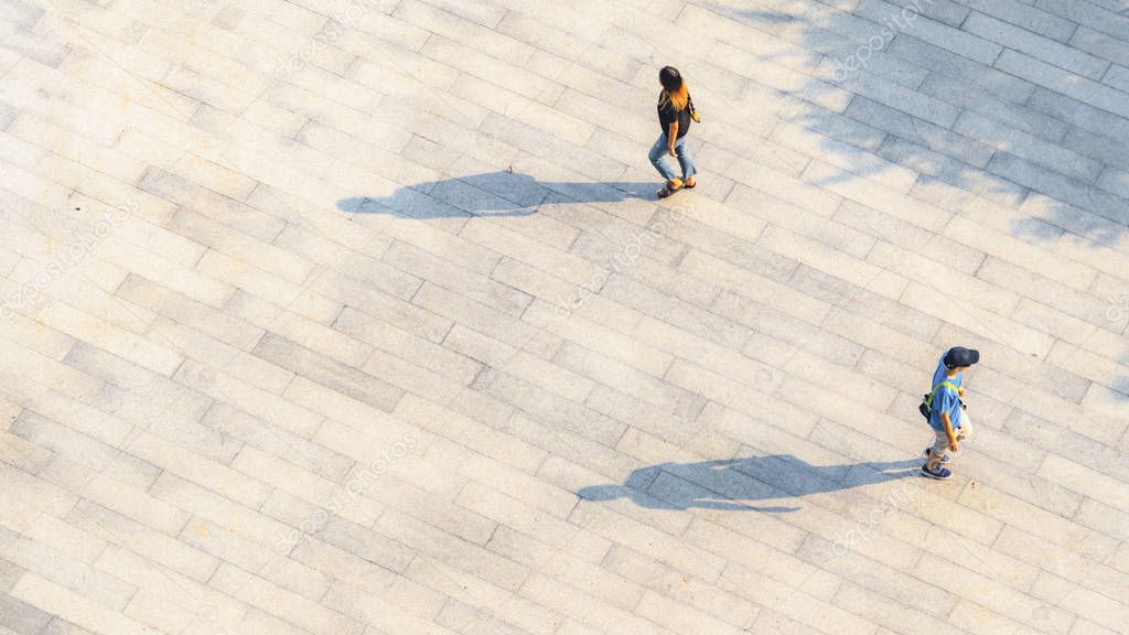 people walk on across the pedestrian concrete landscape with black silhouette shadow on ground (top aerial view)