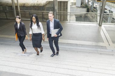 Çok uluslu iş adamlarından oluşan üç kişilik bir grup. Takım elbiseli kadın ve erkek, yaya geçidinde yürüyorlar.