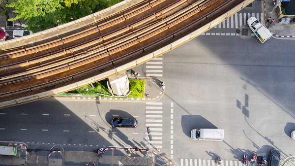 Top view aerial of a driving car on asphalt track and pedestrian crosswalk in traffic road with light and shadow silhouette with rail sky train.