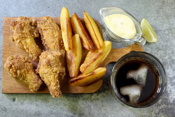 Fried chicken wings on concrete table. Breaded Crispy fried chicken wings with French fries with cheese sauce and soda