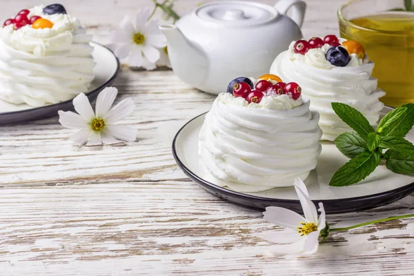 Delicious mini Pavlova meringue cake decorated with fresh red currant and blueberry whith tea on white background. Selective focus