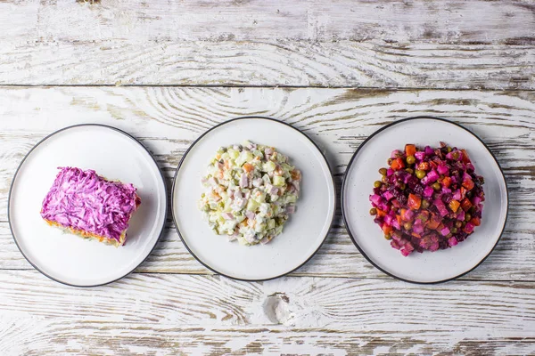 Russian food on wooden background. Assortment salad of Russian cuisine - Olivier salad, vinaigrette - beet salad, herring salad. Top view. Copy space.