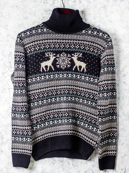 Warm black Christmas sweater with deers on hanger on white background.